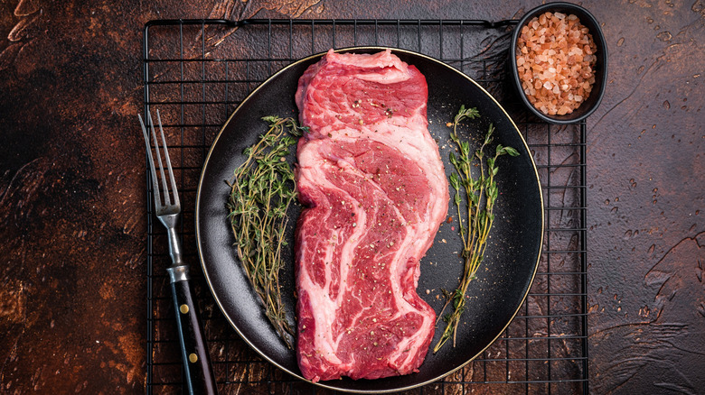 Raw chuck eye steak on cutting board with herbs and seasonings