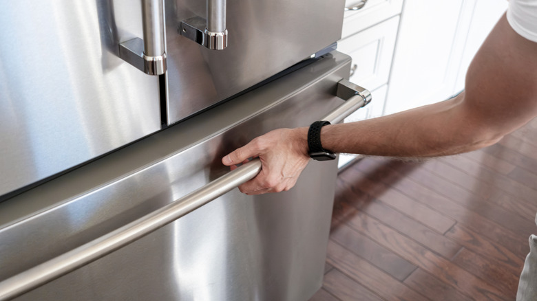 Hand on the handle of a stainless steel freezer drawer