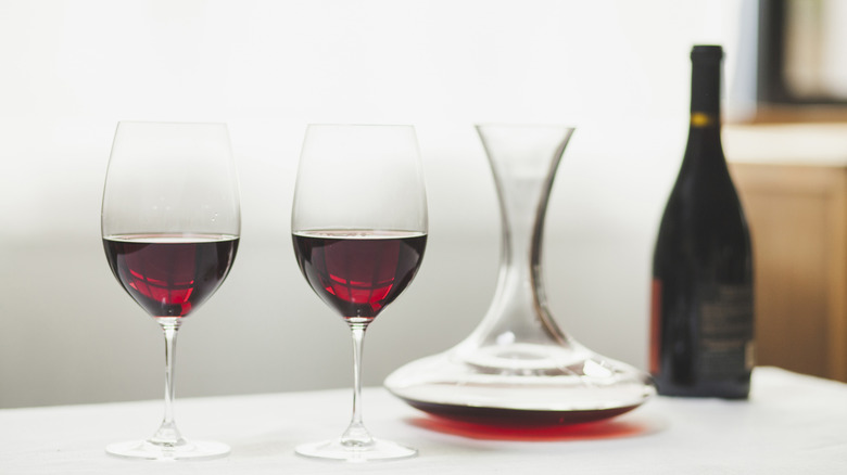 Two glasses of red wine next to a decanter and wine bottle