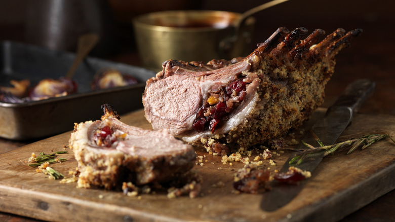 A cooked rack of lamb with a crust on a cutting board