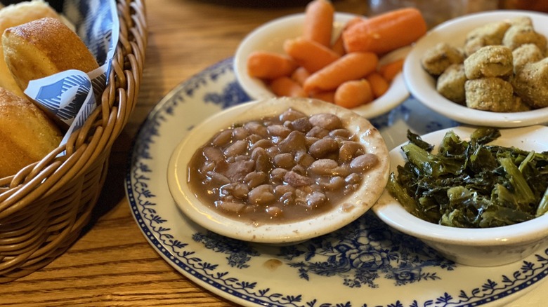 Country vegetable plate of pinto beans, turnip greens, carrots, and fried okra next to corn muffins