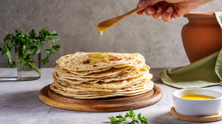 Pouring ghee onto stack of roti