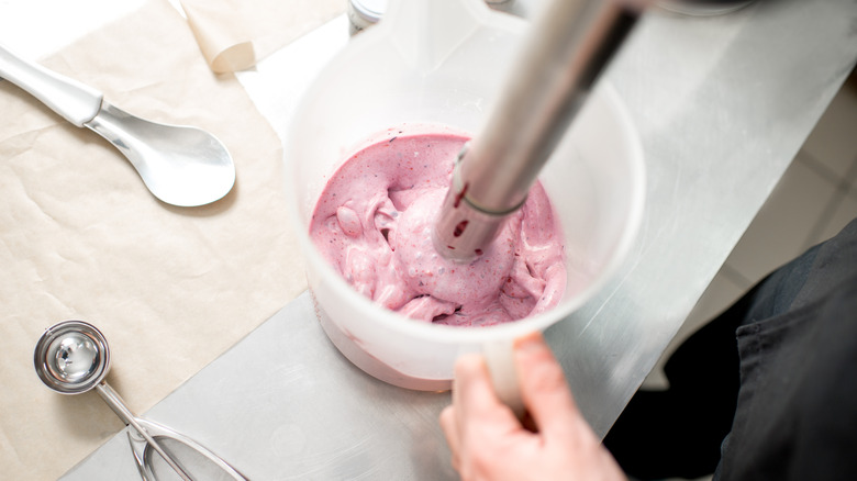 Closeup of person mixing strawberry ice cream with an immersion blender