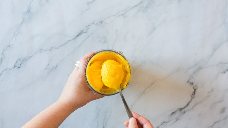 Hand lifting pumpkin puree from cup