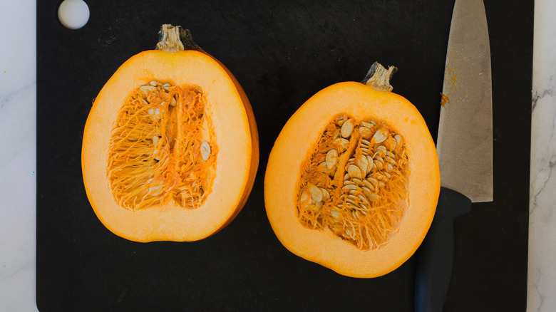 Two pumpkin halves and a knife on baking sheet