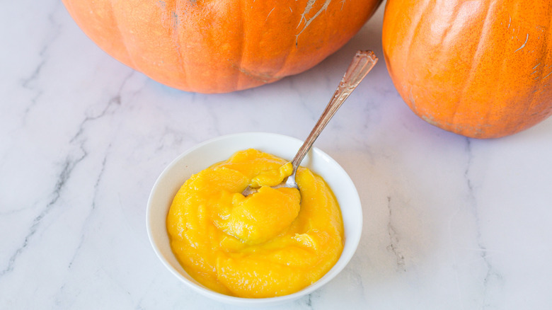 pumpkin puree in a bowl with pumpkins in background