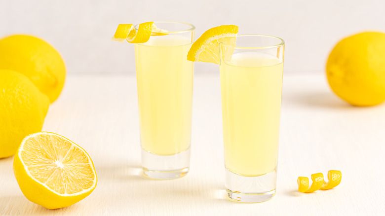 two shot glasses with a yellow drink inside and lemons around it