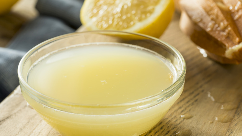Glass bowl of lemon juice with lemon in background