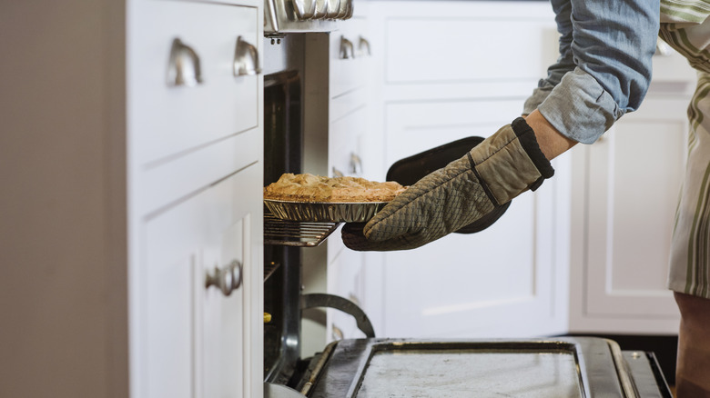 A person removes a pie from the oven in profile.