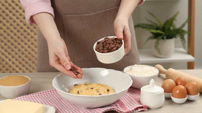 Hands add chocolate chips to cookie dough