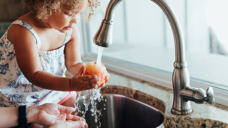 Girl rinsing an apple in the sink