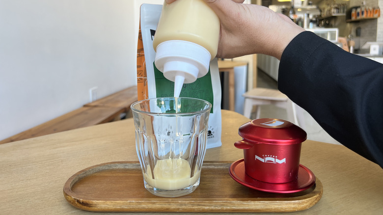 Hands pouring condensed milk into glass