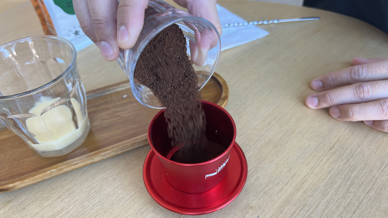 Hand pouring ground coffee into filter