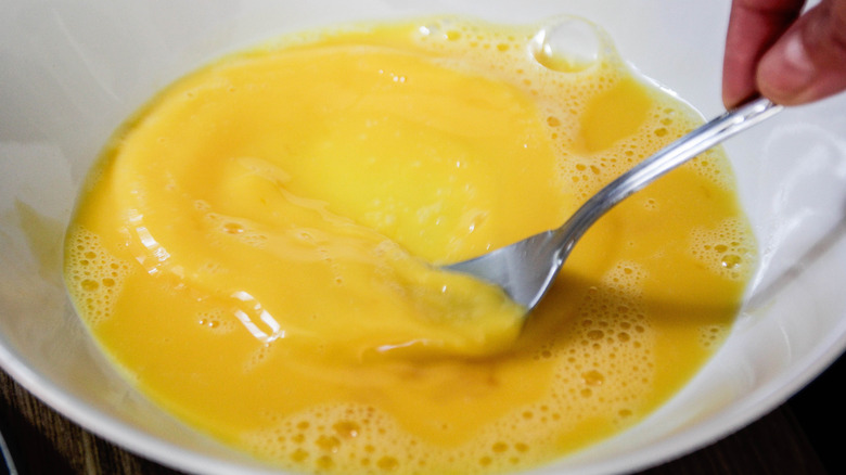 Hand beating eggs in a white bowl with a fork