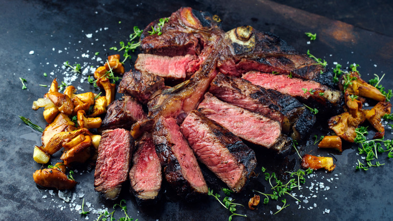 Sliced porterhouse steak with mushrooms, salt, and fresh herbs