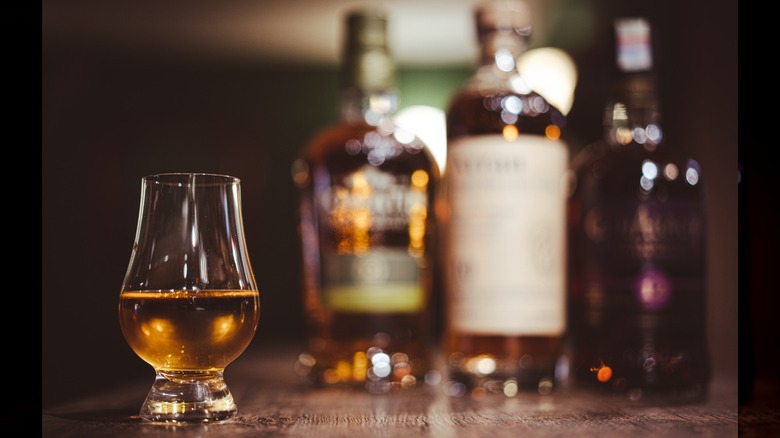 A glass of whiskey with several whiskey bottles