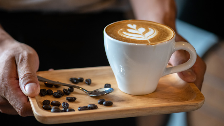 A latte with rosette art sits on a tray with coffee beans.