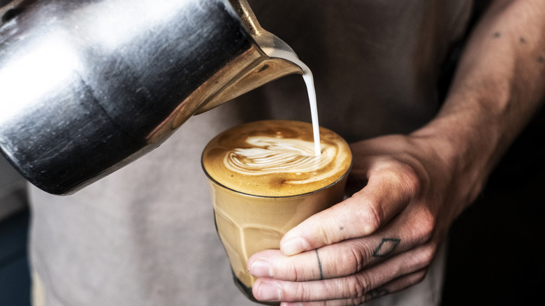 A person pours milk into an espresso to create latte art.