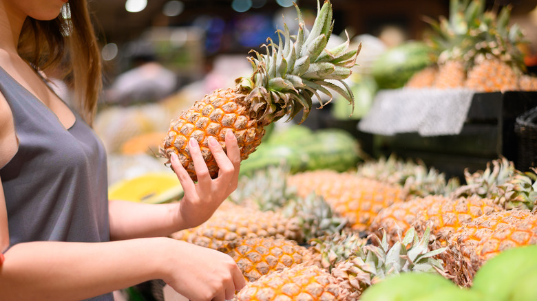 person picking out pineapple at store