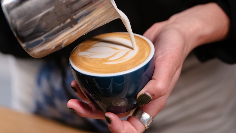 Barista pouring milk into hot café latte