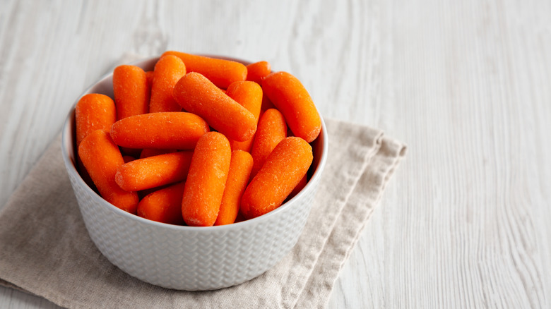 Baby carrots in a white bowl on a towel