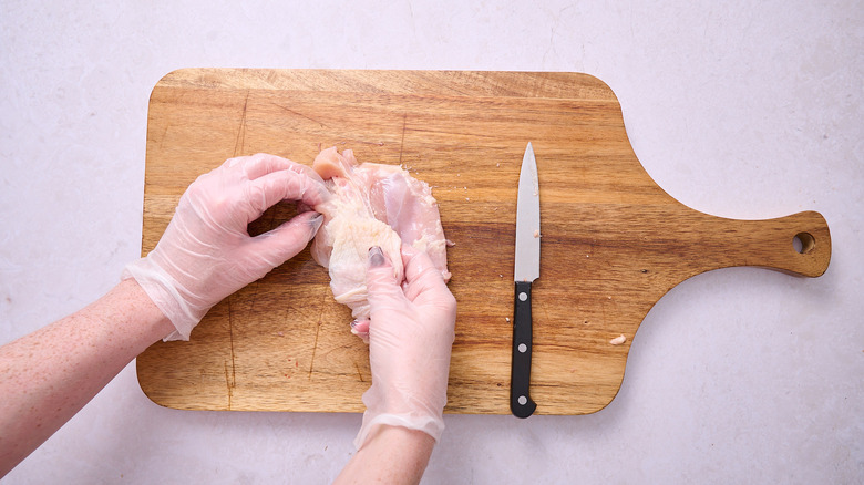 A hand removing chicken skin from a thigh