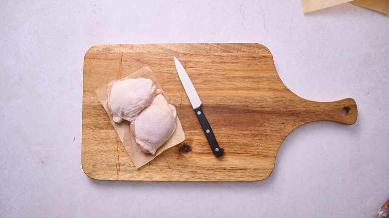 Chicken thighs and a knife on a cutting board