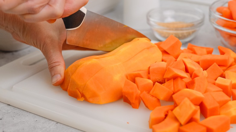 Person slicing orange butternut squash into cubes