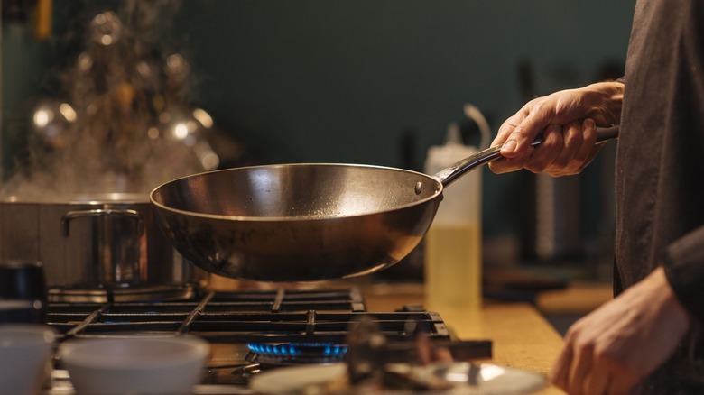 chef holding wok over stove