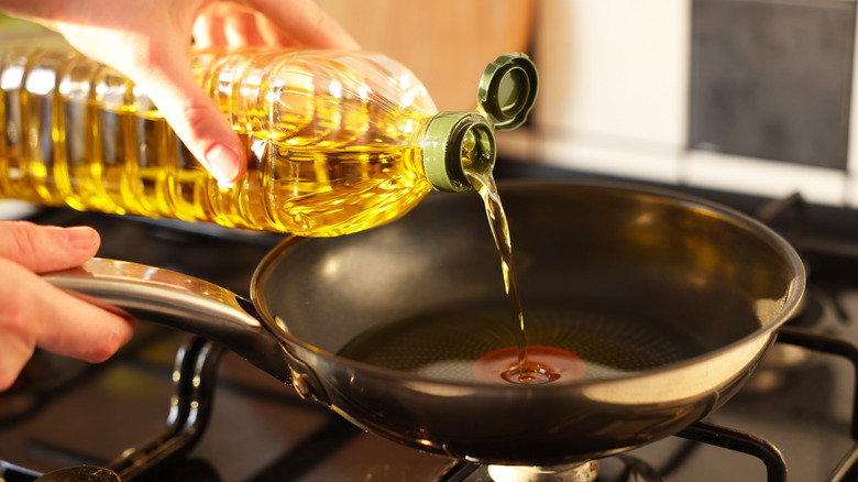 Hands pouring vegetable oil into a pan