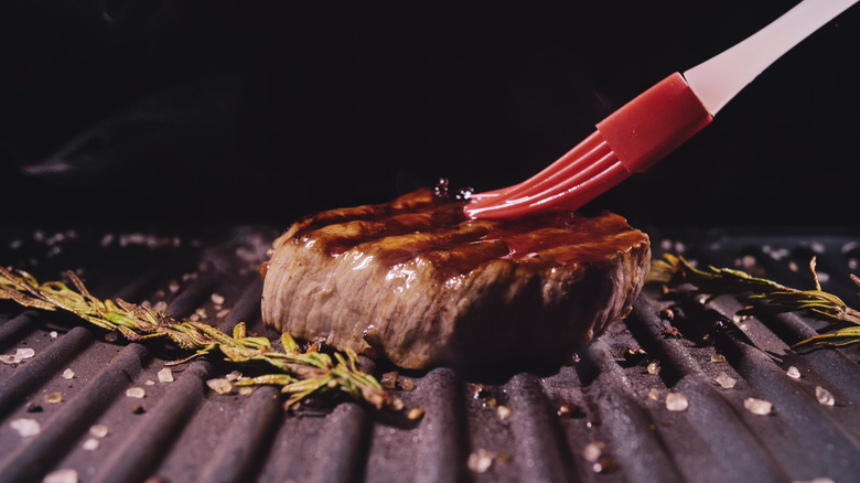 A steak on a grill top is brushed with sauce