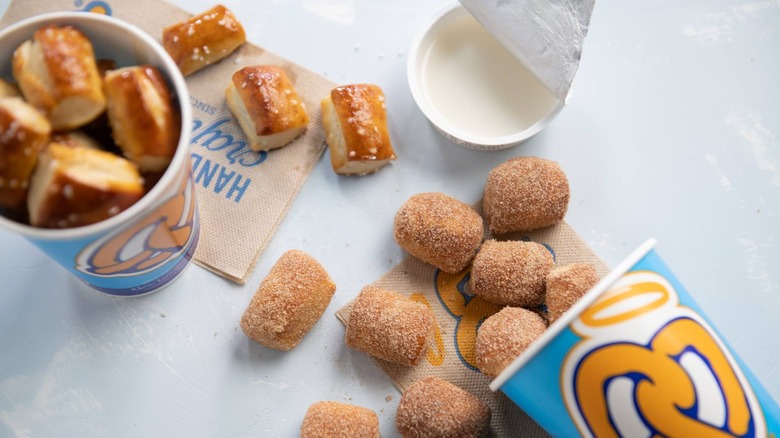 cups of original pretzel bites and cinnamon sugar bites spilling out of cup with sweet glaze dip beside them