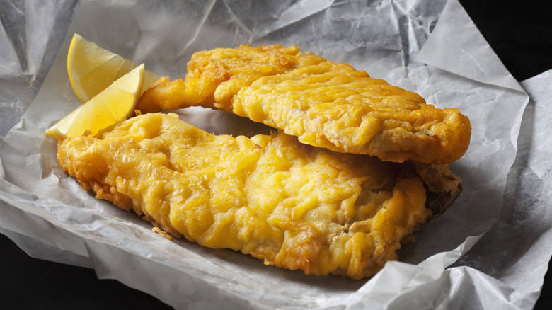 Crispy fried fish with lemon wedges on paper