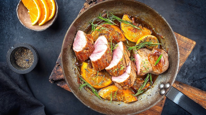 Sliced pork tenderloin in skillet with fresh herbs and sliced oranges