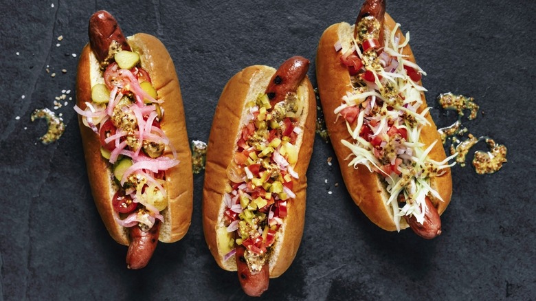 three hot dogs with the works on a slate background