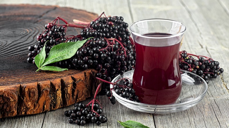 glass filled with elderberry syrup beside elderberry bunches on wooden decorative piece