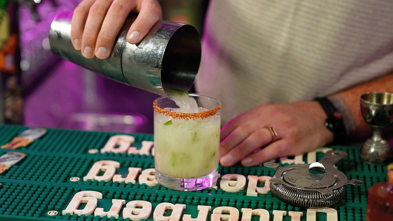 Pouring a margarita into a glass with a Tajín-salted rim