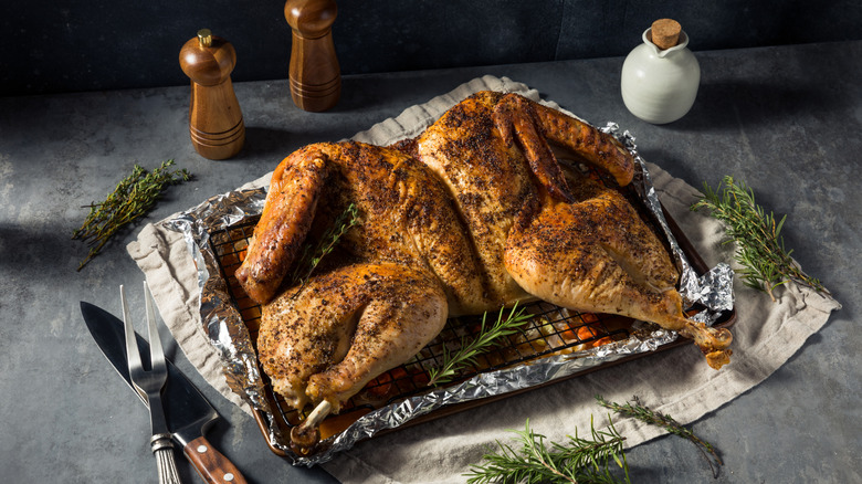 Spatchcocked turkey on an aluminum foil lined pan with rosemary