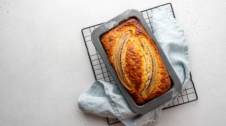 A loaf of banana bread on a kitchen towel that's placed on a wire rack