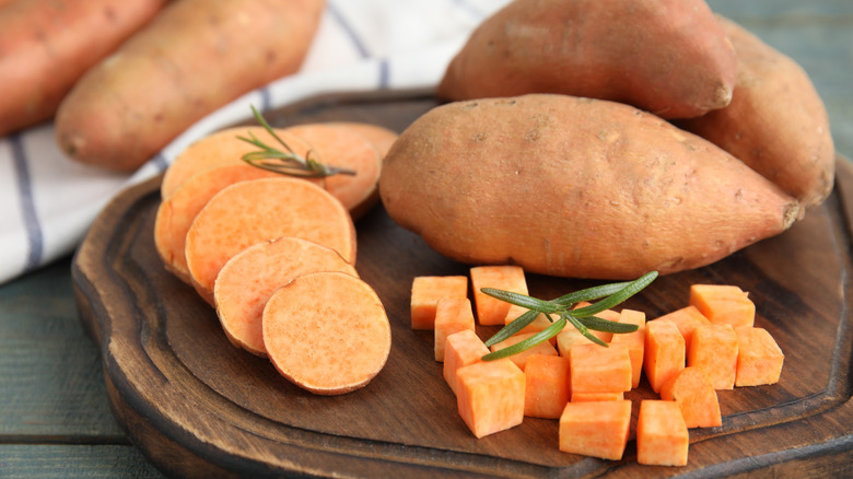 whole, sliced, and diced raw sweet potatoes on a wooden board