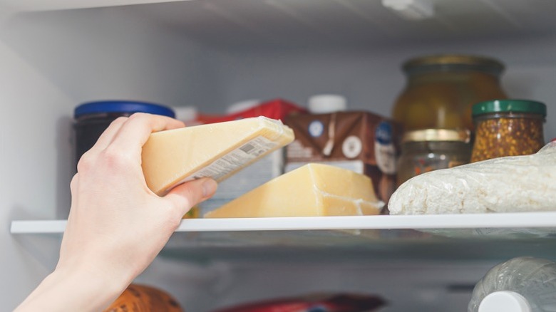 Placing a wedge of cheese onto a refrigerator shelf