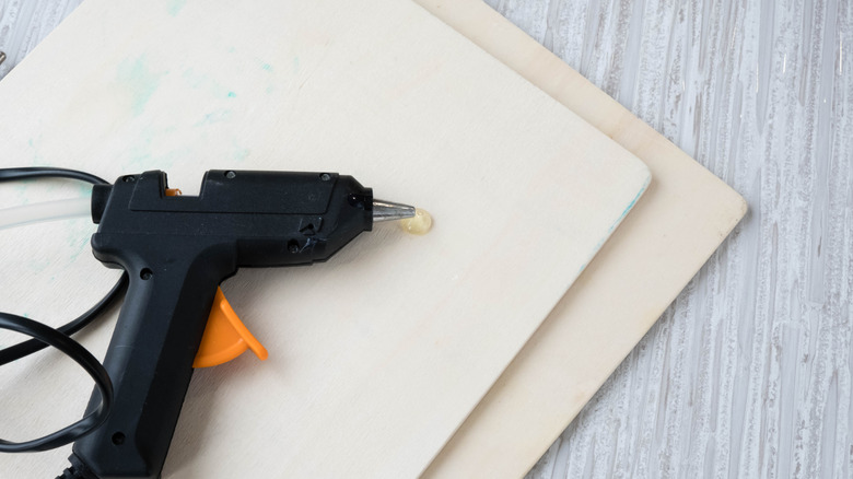 Hot glue gun resting on a wooden sheet