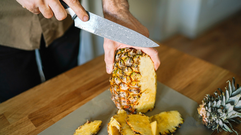 person cutting the skin off a pineapple