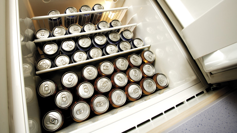 Many beer cans lining the inside of a refrigerator.