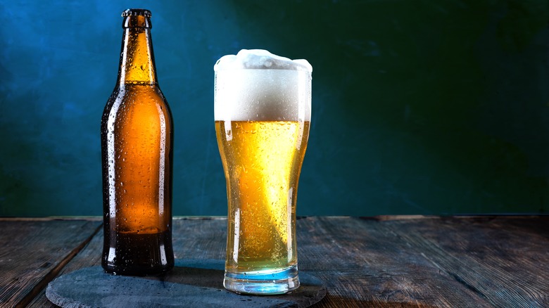 A brown bottle of beer beside a glass of foamy beer.