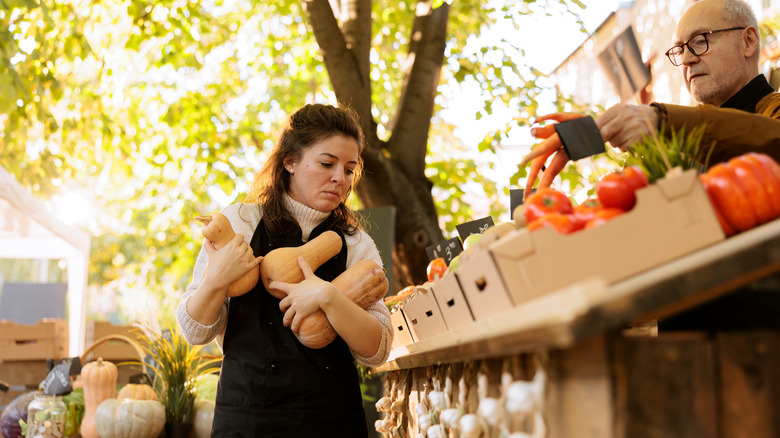 A woman at an outdoor market holding three butternut squash