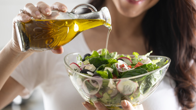 Woman pouring bottle of olive oil onto a salad