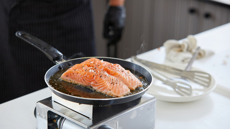 salmon cooking in pan with chef in the background