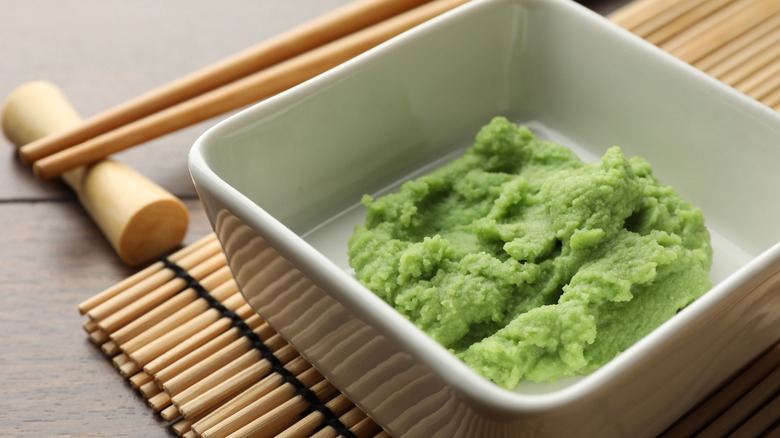 wasabi in square white dish with wooden chopsticks beside it