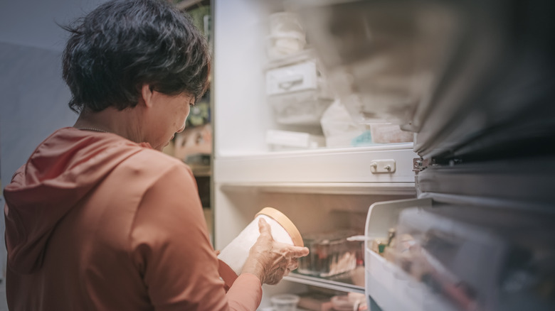 A woman looking at a pint of ice cream in front of a freezer